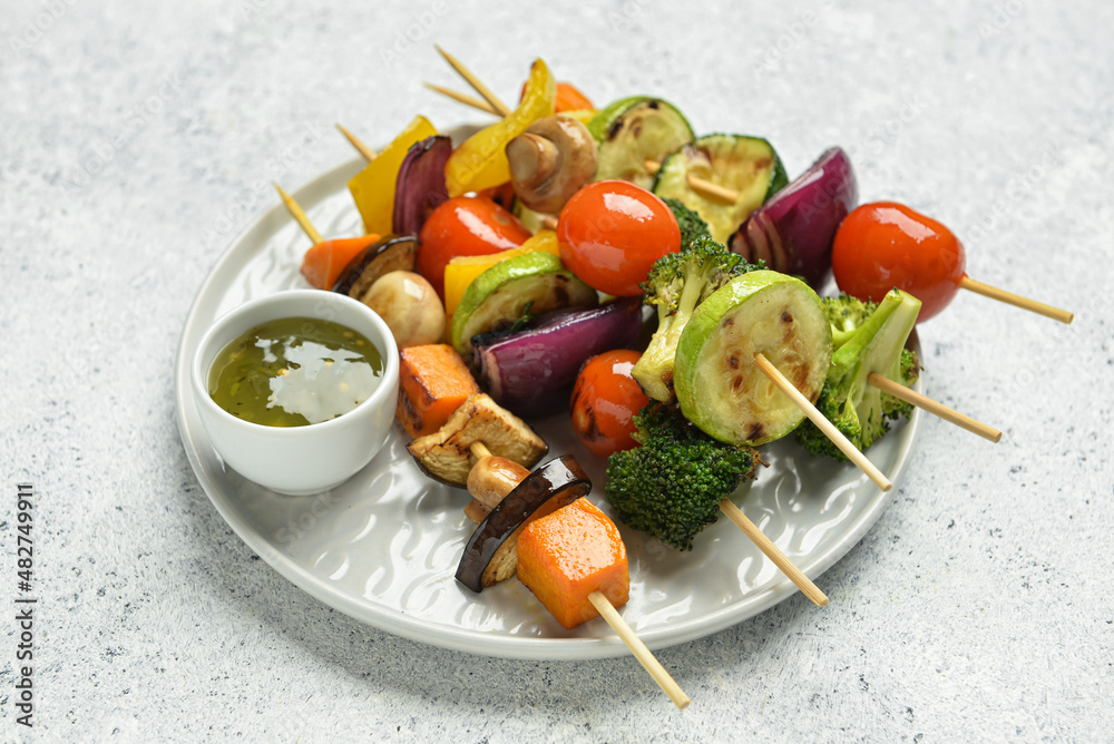 Plate with tasty vegetable skewers and sauce on light background