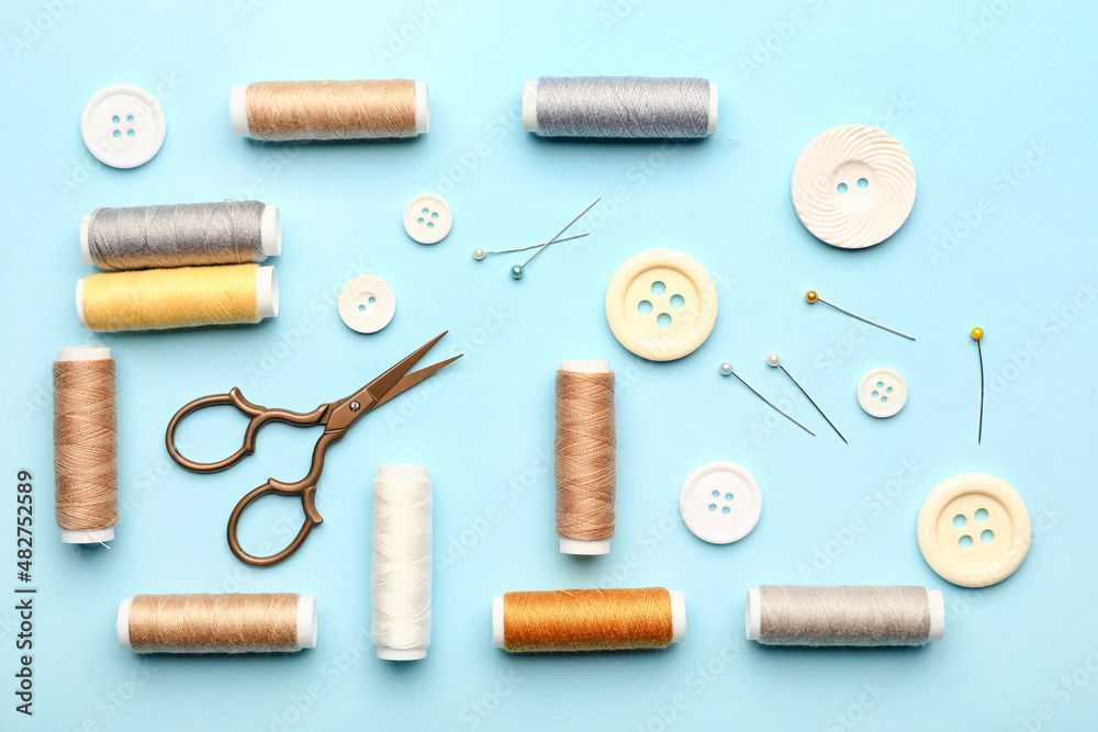 Sewing thread spools, buttons, scissors and pins on color background