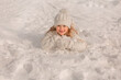 a beautiful happy smiling blonde girl lies on the snow in a knitted white hat and sweater and a fur winter vest