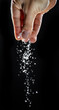 Male hand sprinkling edible salt at black background.