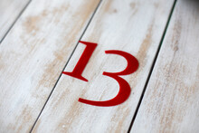 The Number Thirteen Is Written In Red Letters On A Light Wooden Table.