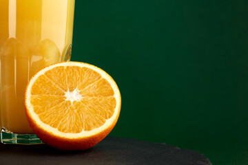 Wall Mural - Sliced orange and a glass of orange juice on a dark background. The glass is not fully visible