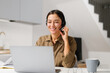 © Face Stock - Young cheerful woman using headset for online talking sitting at the desk at home office. Pleasant female operator looking at the screen. Remote work concept