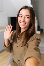 Happy Asian Woman Holding Smartphone And Waving With Hand To The Camera While Having Video Call With Somebody. People And Technologies Concept