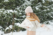 © Dina - Happy woman in winter forest during snowfall, enjoying winter. Millennial young woman with long hair in beige warm outfit walking in the snowy park in nature near fir trees, being careless and free..