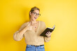 Young beautiful woman wearing casual sweater with a book in hand over isolated yellow background amazed and pointing the notebook