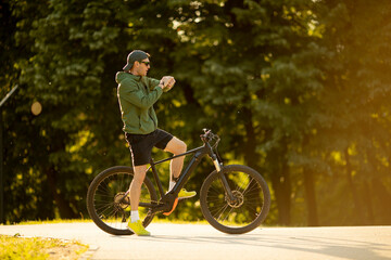 Wall Mural - Young man checking time on ebike in nature