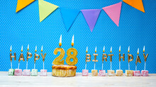 Congratulations On Your Birthday From The Letters Of The Candles Number 28 On A Blue Background With Polka Dots White Copy Space. Happy Birthday Muffin With Burning Golden Color Candle For Twenty Eigh
