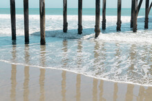 Pier Pilings Reflected On A Wet, Sandy Beach In San Simeon, California