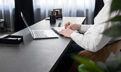 Poster - Man writing in notebook, using laptop at office desk.