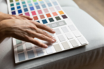 Unrecognizable female hands on paint swatches palette close up. Fashion designer woman use pantone samples choose color prepares for coming repairs works selecting wall colour, home renovation concept