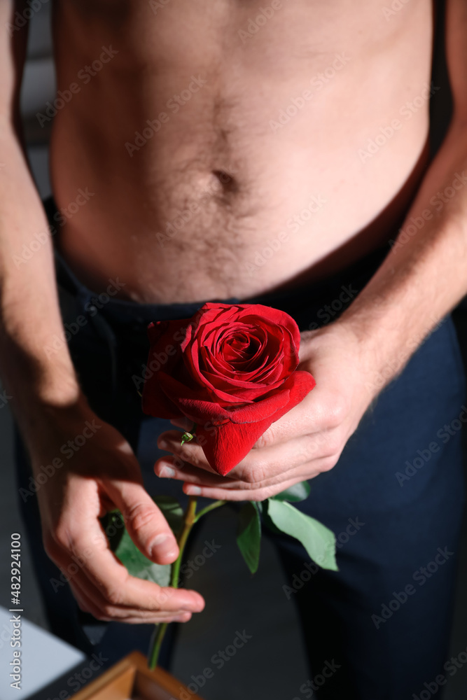 Young man holding red rose, closeup. Erotic concept