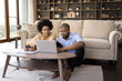 © fizkes - African couple sit in living room discuss receipts, control family budget, calculate household bills to pay, utility expenses, make payment via e-bank app on laptop, accounting, money control concept