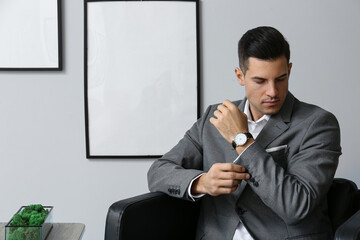 Handsome man in elegant suit sitting in armchair and adjusting sleeve