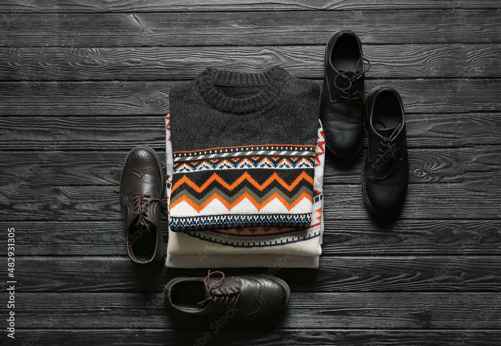 Stack of male sweaters and shoes on dark wooden background