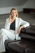 © InfiniteStudio - young woman in a white business suit talking on a mobile phone while sitting on a leather sofa. Portrait of business woman smiling