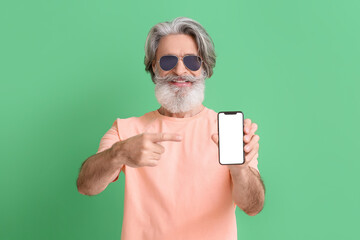 Canvas Print - Senior man in sunglasses pointing at mobile phone on green background