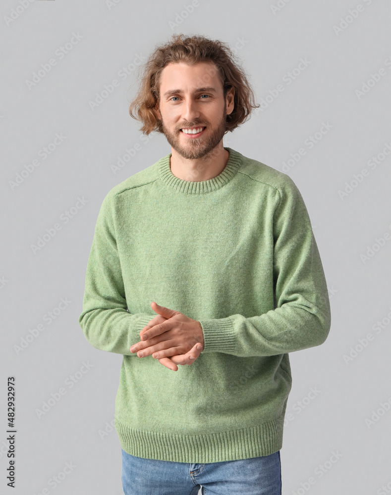 Handsome young man in knitted sweater on grey background