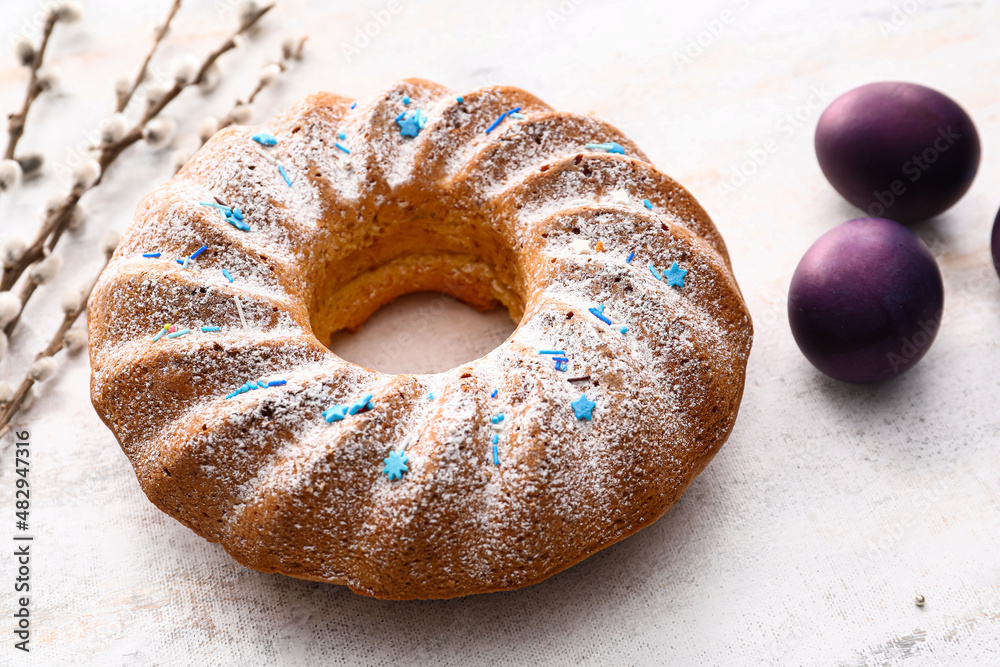Tasty Easter cake and eggs on light background