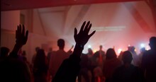 Hands Of Female Christian Worshiping And Praising While Singing On Youth Festival Concert. People With Raised Arms On Music Live Event With Lights. 4K Back View Handheld Shot In Slow Motion