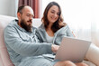 © Beton Studio - Young beautiful married couple are sitting on sofa at home interior using laptop. Happy smiling Woman and man do shopping online via internet on laptop. Love harmony in relationship.
