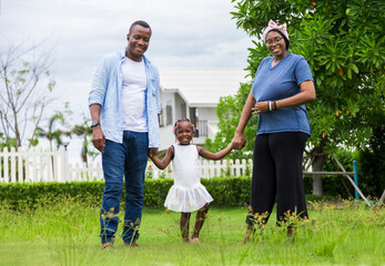 Wall Mural - Happy family of African American people with young little daughter walking on green grass field while enjoying summer garden outside the house in the neighborhood