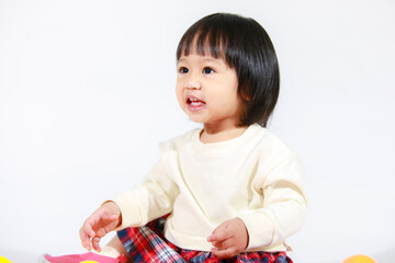 Wall Mural - Studio shot of little cute short black hair Asian baby girl daughter model in casual plaid skirt sitting on floor smiling laughing playing with colorful round balls toy alone on white background