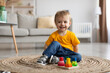 Portrait of adorable toddler boy playing with educational wooden sorting toy, sitting on carpet, free space