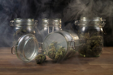 Wall Mural - Cannabis buds spilled on the table from a storage glass jar, filled with smoke.