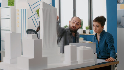 Poster - Team of architects designing building model on laptop in architectural office. Man and woman analyzing blueprints and using computer to plan construction layout and structure.