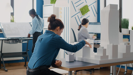 Poster - Man and woman working together with blueprints plans and building model for urban project. Workmates designing construction layout and structure to create architectural development.