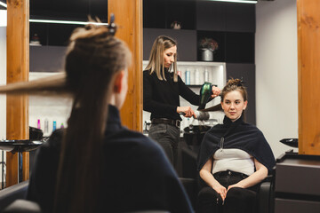 Canvas Print - Master woman hairdresser dries the girl's hair with a hairdryer after washing in a beauty salon.