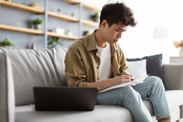 Man holding paper, writing and working on laptop at home