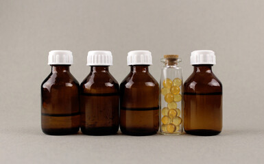 Four dark glass bottles with liquid medicine and one bottle with yellow capsules on a gray background