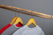 Clothes made of natural cotton hang on wooden hangers on a crossbar made of a stick. The concept of eco-clothing in gray and red