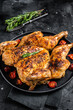 Tobacco whole chicken on plate with herbs and tomato. Black background. Top view