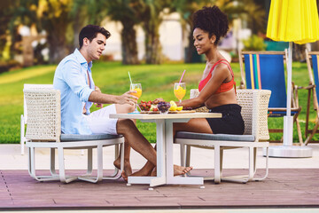 multiracial couple eating healthy fruit breakfast at luxury resort - honeymoon vacation at hotel restaurant poolside