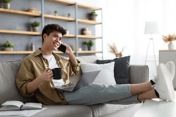 Wall Mural - Cheerful asian guy working and talking on phone at home