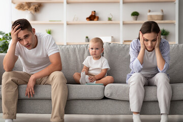 Family Conflicts. Cute infant baby sitting between offended parents after quarrel