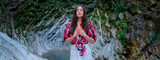 Fototapeta Zwierzęta - Young woman in white dress and plaid shirt practicing breathing yoga pranayama outdoors in moss gorge. Unity with nature concept.