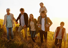 Together Every Step Of The Way. A Multi-generational Family Walking Up A Grassy Hill Together At Sunset.