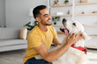 © Prostock-studio - Happy young Arab man stroking his adorable dog in living room. Human animal friendship concept