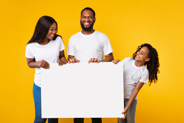 Wall Mural - Black family holding blank white advertising billboard at yellow studio
