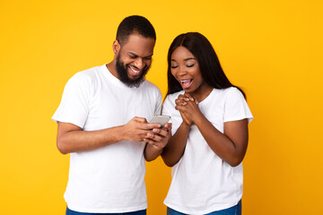 Wall Mural - African american couple using smartphones, yellow studio wall