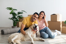Full length portrait of happy young diverse couple with their dog posing on floor of new home on moving day