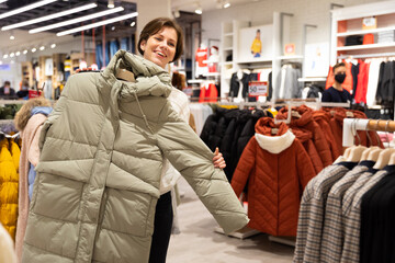 Wall Mural - Photo of young attractive brunette woman with a short haircut in a white sweater chooses stylish and casual winter clothes in a store in a shopping centre