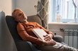 Tired mature man sleeping at the armchair with book on chest after reading