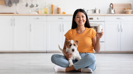 Wall Mural - Cheerful asian lady with cute doggy showing pets supplement jar