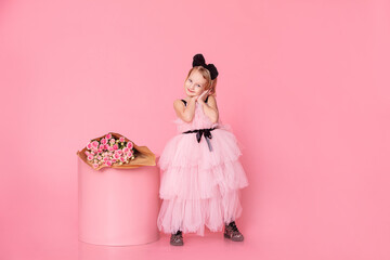 Child girl in a pink dress on a pink background, with a bouquet of roses, fashionable, stylish and cheerful