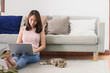 © interstid - Asain woman smiling while using laptop for working in living room with her cat lying by her side . Working at home concept